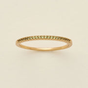 A gold ring featuring a single row of small round-cut light green gemstones, photographed on a clean, solid, warm off-white background.