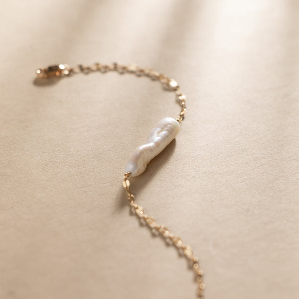 Gold bracelet with a baroque pearl pendant against a plain beige background.