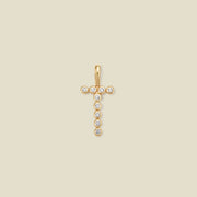 A gold initial 'T' charm comprised of clear round bezel-set gemstones, set against a solid beige background.