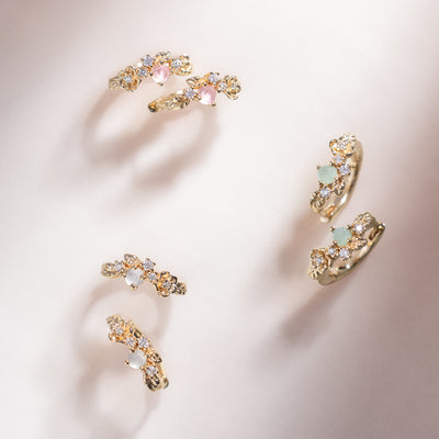 Three sets of gold hoop earrings with florals and green, pink and white prong-set stones.
