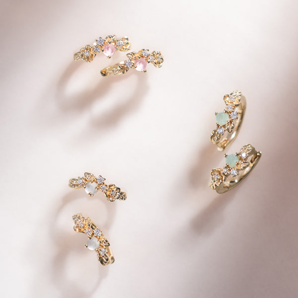 Three sets of gold hoop earrings with florals and green, pink and white prong-set stones.