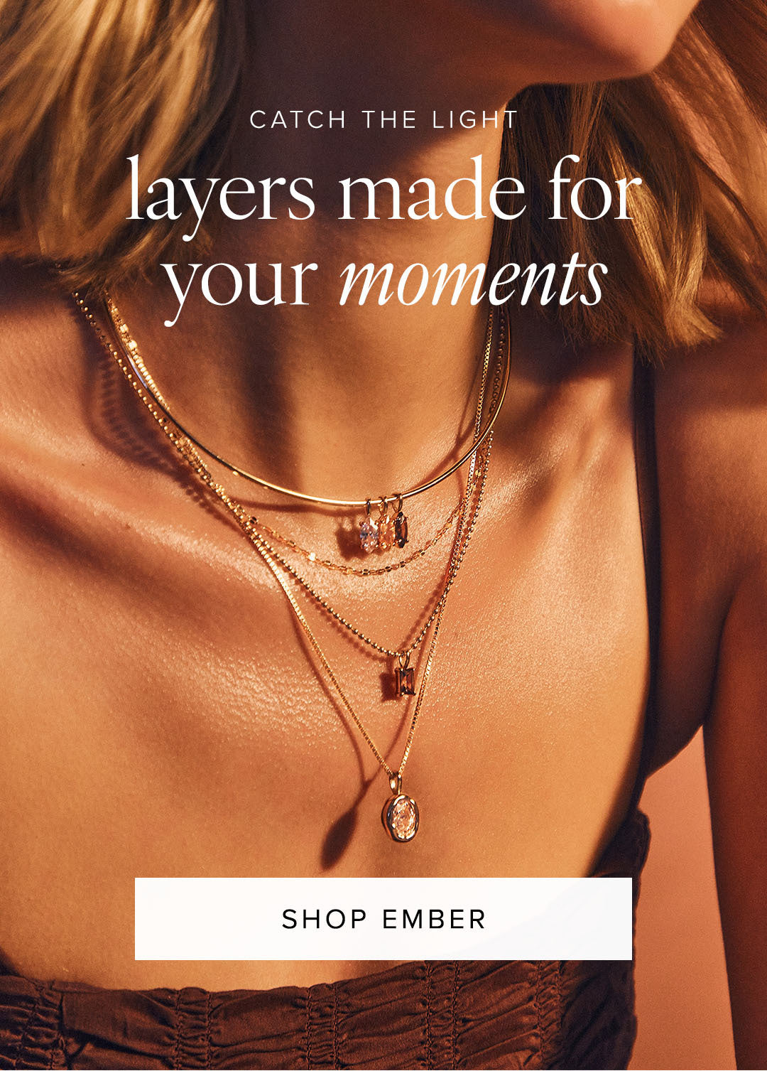 A close-up lifestyle shot of a model wearing layered gold necklaces, including a delicate chain, a chain with a small pendant, and a longer chain with an oval pendant. The image has warm, golden lighting and text overlays reading 'CATCH THE LIGHT layers made for your moments' and 'SHOP EMBER'.