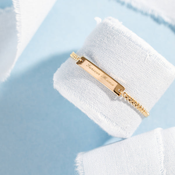 Gold bracelet with engraved name on a white fabric background