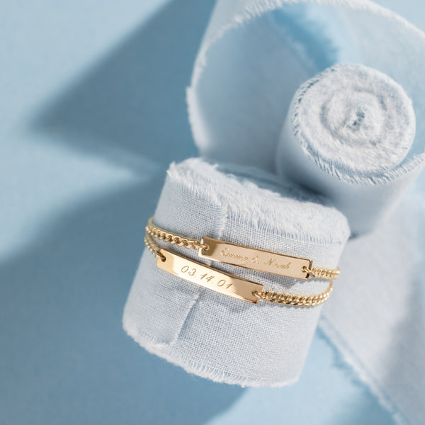 Two Gold bracelets on a blue textured background with engraved names and date
