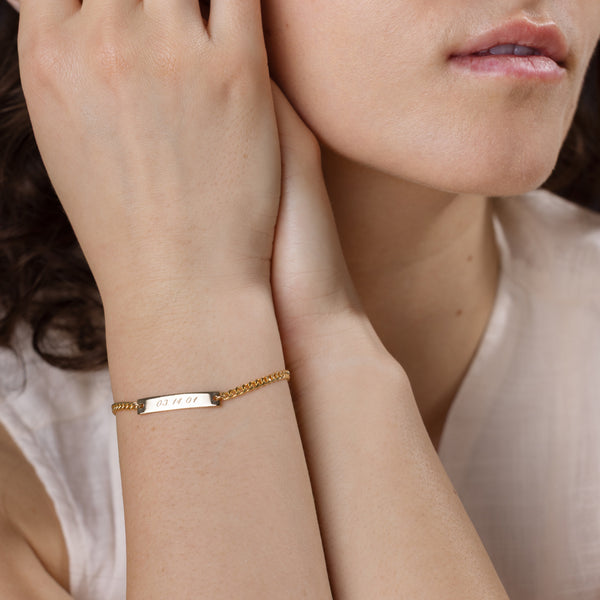 Close-up of a woman wearing a gold bracelet engraved with a date with a soft background