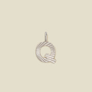 A small silver Q-shaped charm with a textured, sunburst striped pattern, shown on a solid light beige background.