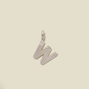 A small silver W-shaped charm with a textured, sunburst striped pattern, shown on a solid light beige background.