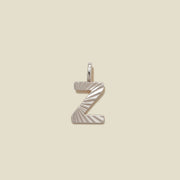 A silver initial 'Z' charm with a sunburst textured pattern, shown on a solid light beige background.