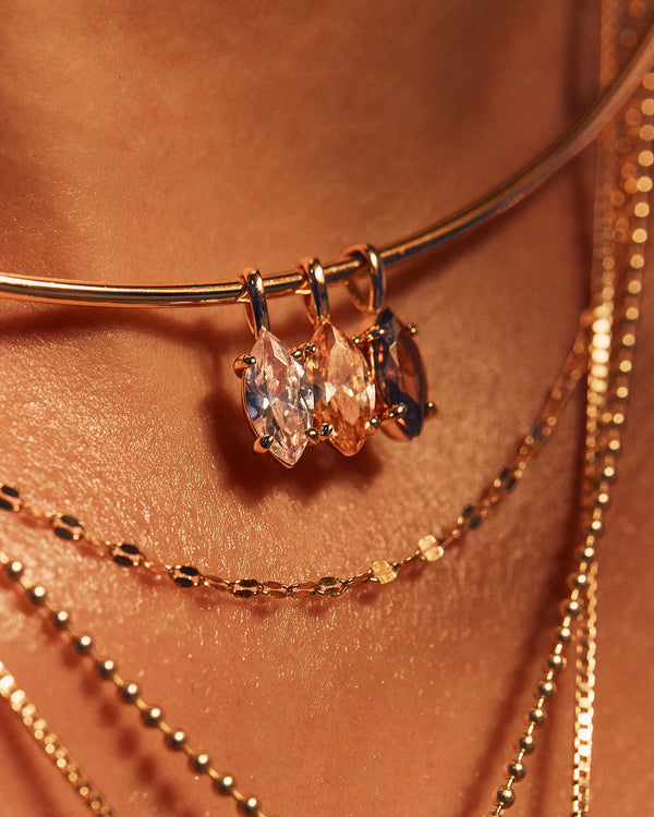 Close-up of a person wearing layered gold necklaces, including a collar necklace with three marquise-cut gemstone pendants and delicate chain layers on warm skin.