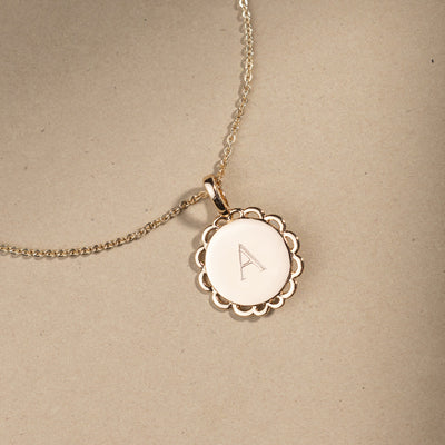 Gold necklace with a round pendant engraved with 'A' on a beige background