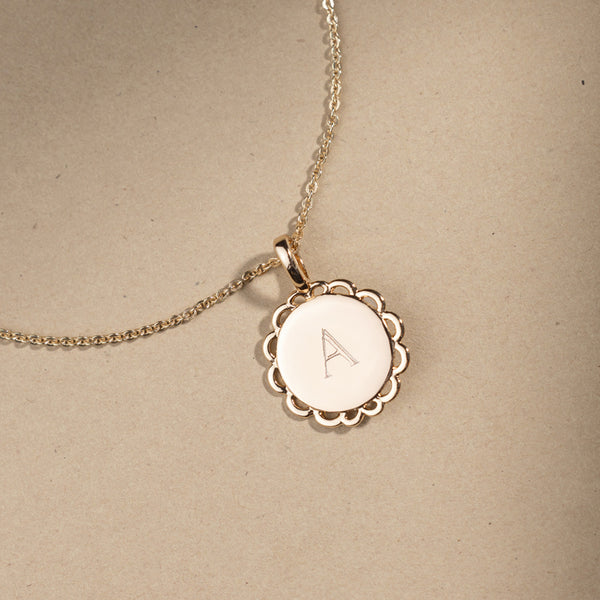 Gold necklace with a round pendant engraved with 'A' on a beige background