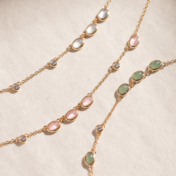 Pink, green, and white bezel-set stone necklaces against a plain beige background.