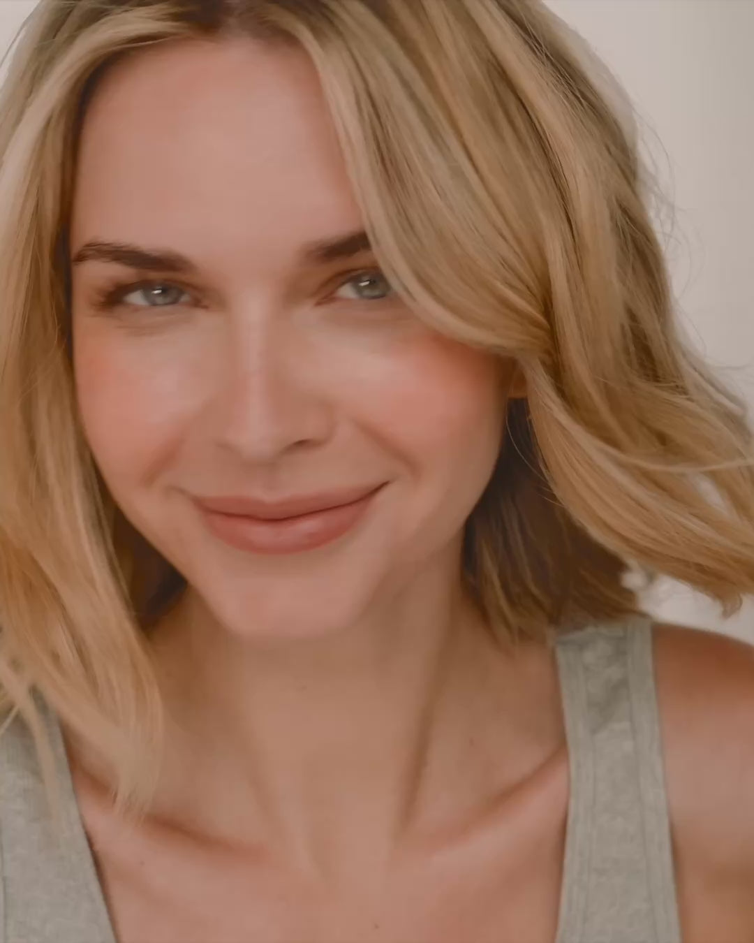 A short close-up video of a playful woman showcasing three different sizes of thin, gold hoop earrings while playing with her hair and smiling.