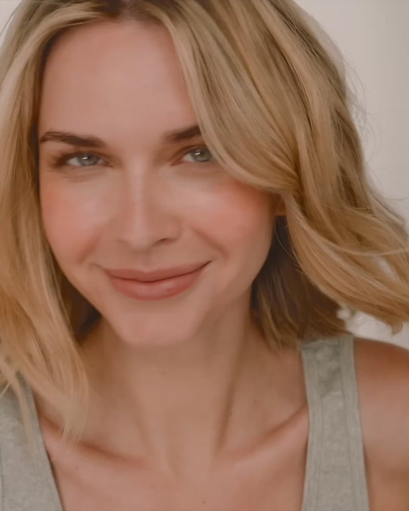 A short close-up video of a playful woman showcasing three different sizes of thin, gold hoop earrings while playing with her hair and smiling.