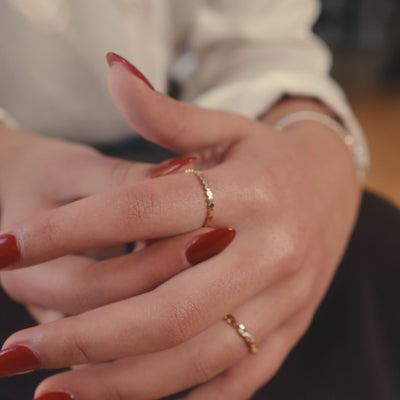 A short, close-up video of a woman putting on and playing with a gold, textured ring on her hand. 