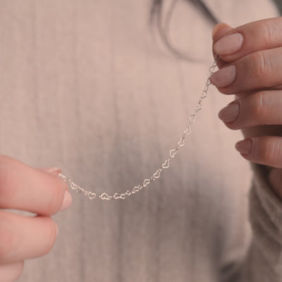 A short video of a person holding a silver heart link chain bracelet in both hands.
