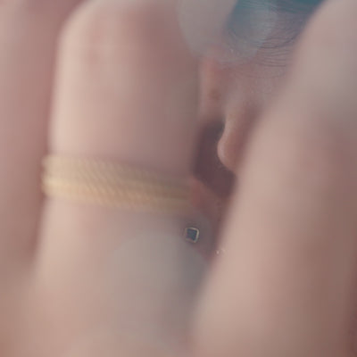 A short video of a person's ear wearing a polished gold hoop earring and two gold studs, both with square bezel-set gemstones in either clear or dark red.
