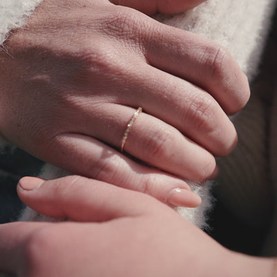 A short close-up video of different shots of a person's hand wearing a delicate gold ring with baguette and round clear gemstones in a morse code pattern.