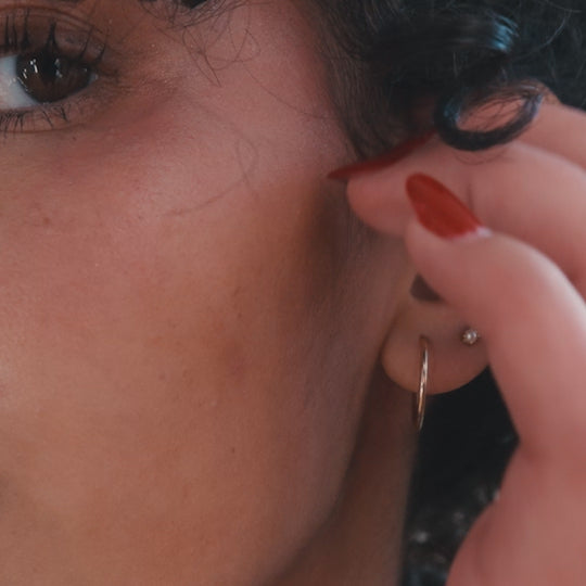 A short lifestyle video of a woman showing a close up shot of her ear with multiple earrings (both hoops and studs), then smiling and shaking her head happily.