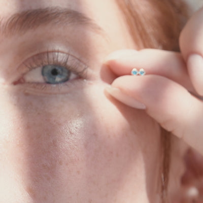 A short video of a woman holding two square bezel-set blue gemstone earrings in her fingers next to her blue eyes.