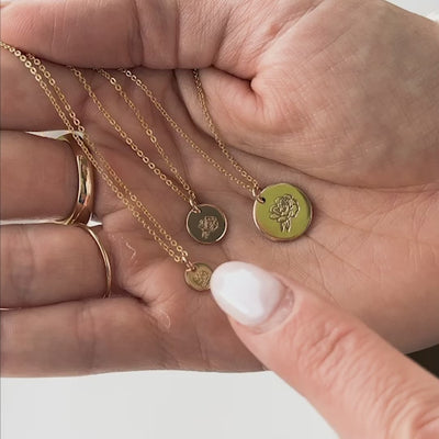 A short video of a hand holding three gold pendant chain necklaces, each in a different size with varying peony flower designs. There is text near each of the necklaces saying '1/4"', '3/8"', and '1/2"'.