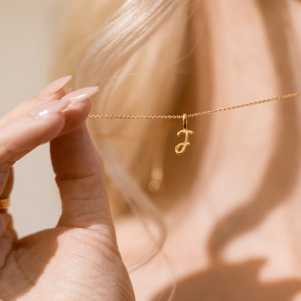 Close-up of a hand holding a delicate gold chain necklace with a small cursive initial  "J" pendant.